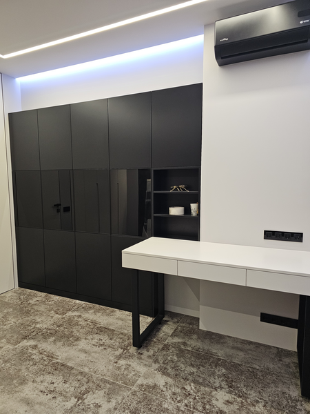 Многофункциональная встроенная система хранения во всю стену: сочетание закрытых чёрных фасадов, зеркальных поверхностей и открытых полок, выполненная на заказ мебель формирует единое архитектурное решение с рабочей зоной и скрытым хранением.