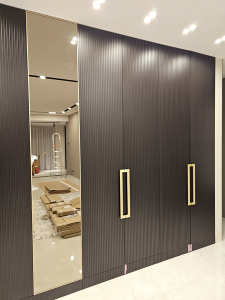 Фрагмент фасадной части корпусного шкафа с глубоким вертикальным рифлением, акцентными металлическими ручками прямоугольной формы и встроенной зеркальной секцией, подчёркивающей масштаб и геометрию пространства