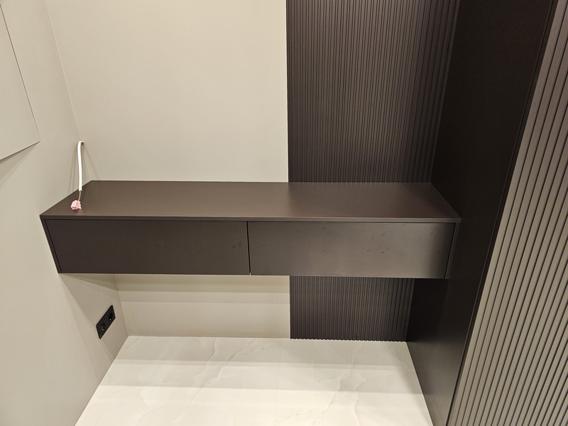 Подвесная консоль из корпусной мебели с двумя выдвижными ящиками без видимых опор, выполненная в тёмном матовом исполнении, интегрированная в систему хранения и визуально объединённая с фасадами шкафа