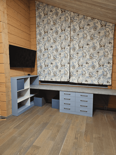 Рабочее место в детской комнате с индивидуально изготовленной корпусной мебелью: столешница во всю стену, выдвижные ящики повышенной вместимости и открытые полки, спроектированные под наклон потолка.