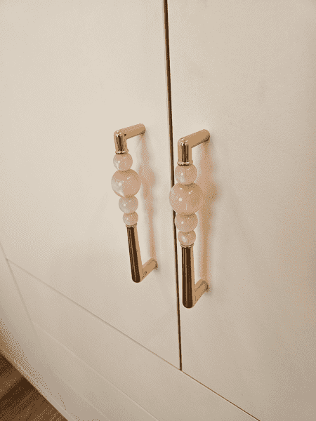 Деталь фурнитуры встроенного шкафа в детской комнате — дизайнерские ручки с декоративными элементами из прозрачных вставок. Ручки выполнены в светлом металлическом оттенке и подчёркивают аккуратный, эстетичный характер мебели. Использование качественной фурнитуры обеспечивает комфортную эксплуатацию и добавляет интерьеру индивидуальности и визуальной лёгкости.