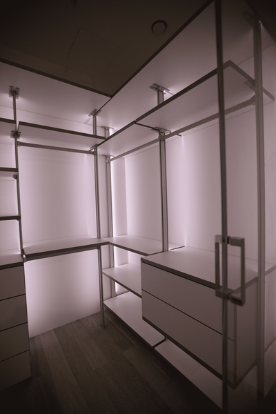 Открытая гардеробная система с прозрачными стеклянными перегородками, равномерной вертикальной подсветкой и симметричной компоновкой модулей хранения с выдвижными ящиками и полками по периметру