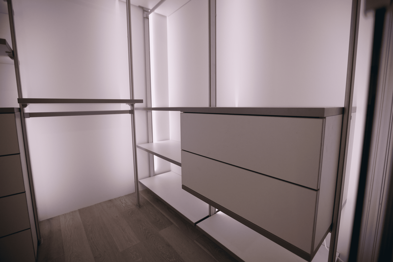 Открытая гардеробная комната с боковым расположением модулей, выдвижными комодами, полками разной глубины и интегрированной подсветкой, подчёркивающей геометрию конструкции