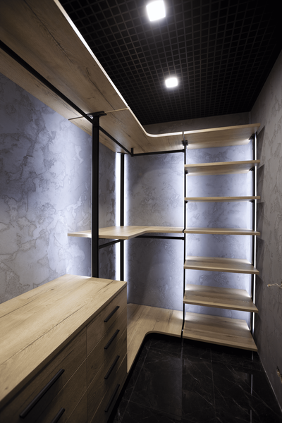 Открытая гардеробная система с чёрным металлическим каркасом и полками под натуральное дерево, встроенная подсветка по вертикалям, угловая планировка с рабочей поверхностью и верхним ярусом хранения.