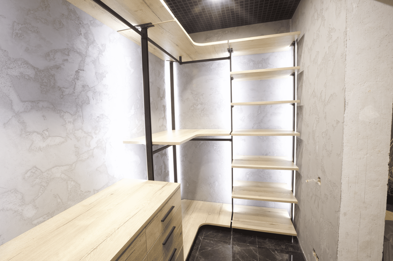 Деталь открытой гардеробной системы с деревянными полками и металлическими стойками, подчёркивающая качество креплений, точность сборки и архитектурный характер конструкции