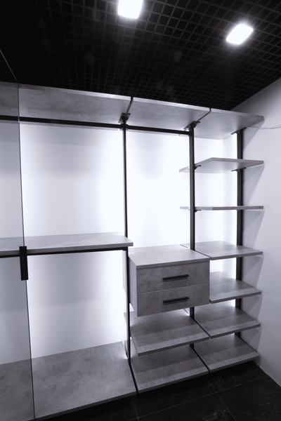 Открытая гардеробная с модульной системой хранения: металлический каркас, полки с отделкой под бетон, выдвижные ящики и нижние секции для обуви, подчёркнутые контурной подсветкой и потолком грильято.