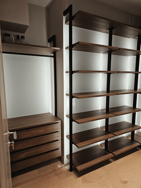 Открытая гардеробная система с металлическим каркасом и деревянными полками, включающая секцию с выдвижными ящиками, высокие стеллажи для хранения и интегрированную подсветку, подчёркивающую геометрию конструкции
