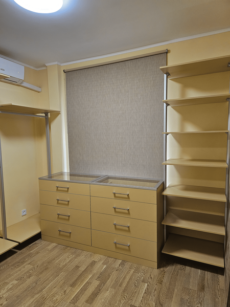 Открытая гардеробная Eureka Stilos с центральным комодом под окном, выдвижными ящиками и симметричной компоновкой секций, выполненная в светлой цветовой гамме для просторных гардеробных комнат