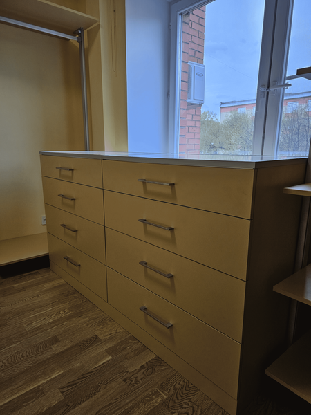 Открытая гардеробная система Eureka Stilos в нише с П-образной планировкой, металлическим несущим каркасом, полками из ЛДСП и центральным комодом с выдвижными ящиками, интегрированная в пространство с окном и естественным освещением