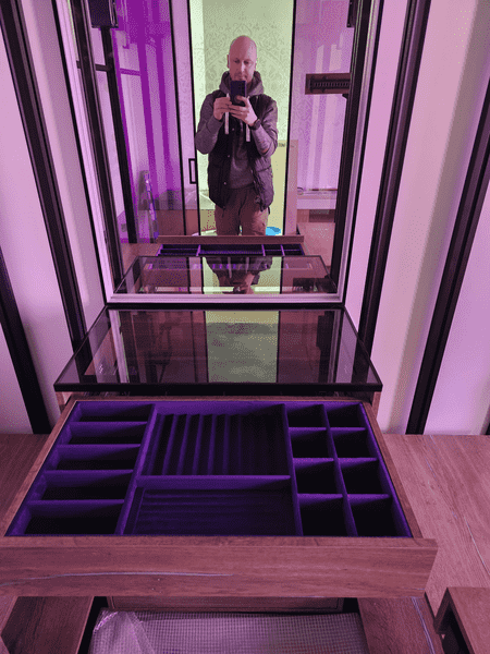 Зеркальная зона гардеробной с центральным комодом и стеклянной поверхностью, комбинирование дерева и металла, мягкая цветная подсветка интерьера