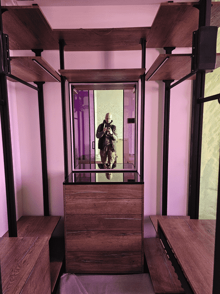 Вид гардеробной через стеклянную перегородку, центральный комод, боковые зоны хранения, сочетание дерева, металла и стекла